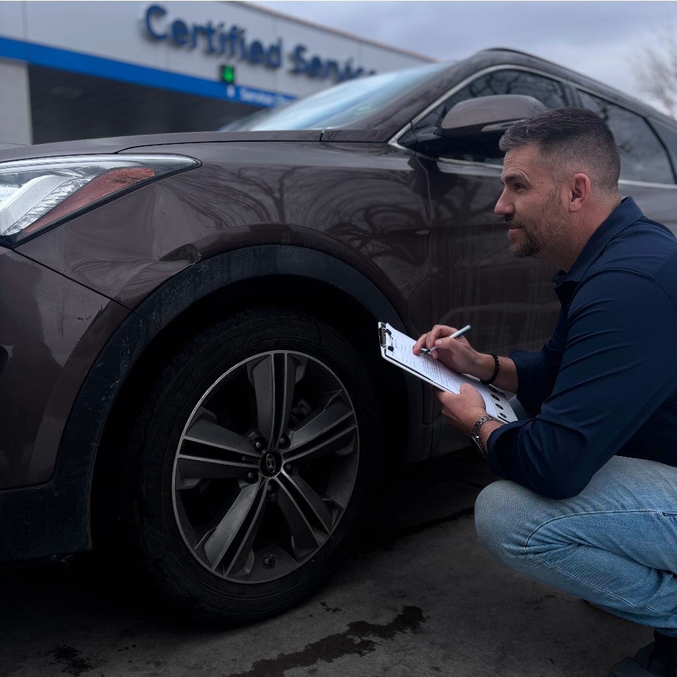 A person uses a specialized tool to pull out a dent on a white car door, with a light reflecting its surface.